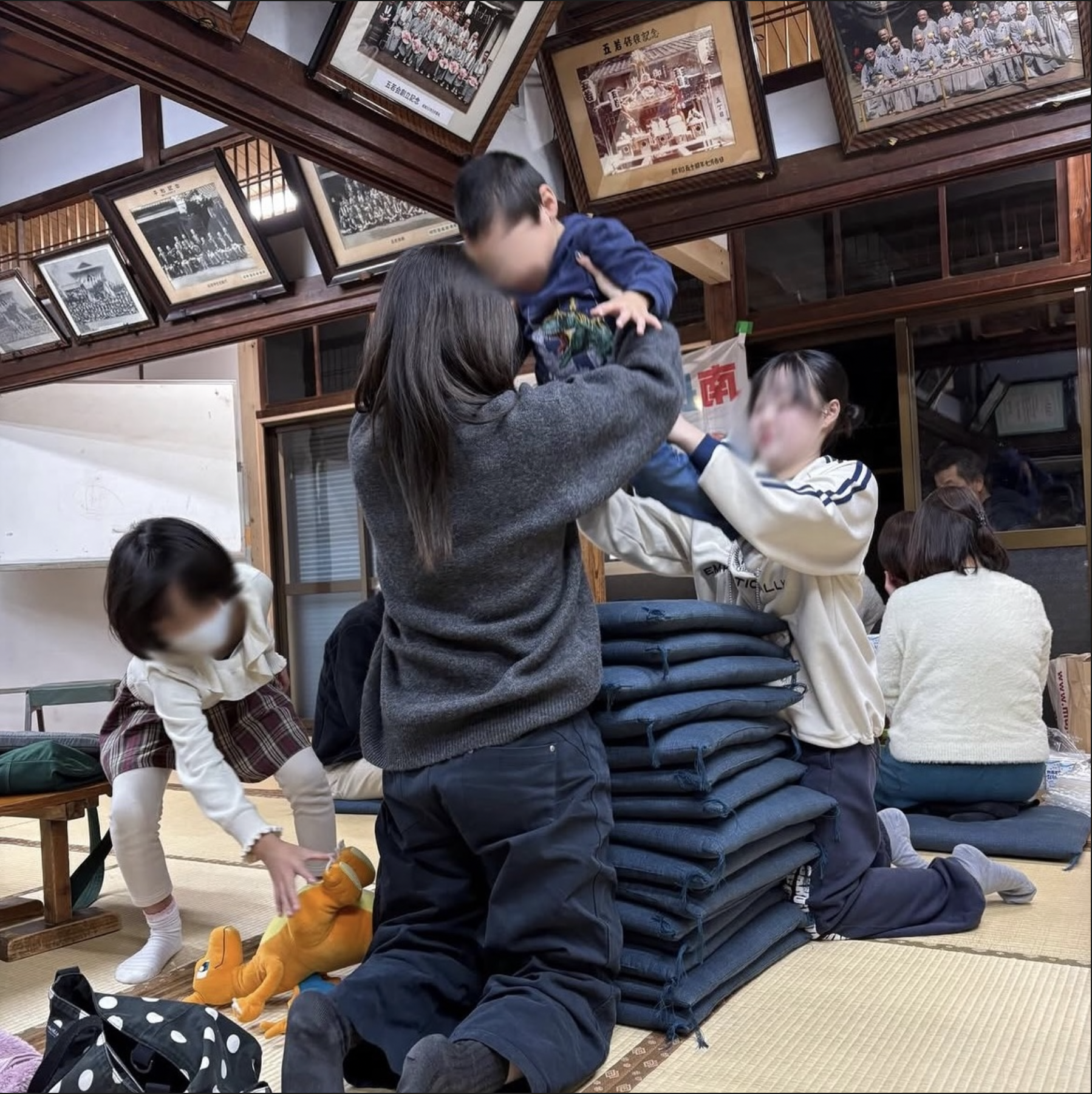 集会所で、スタッフと子どもたちが座布団のそばで遊ぶようす