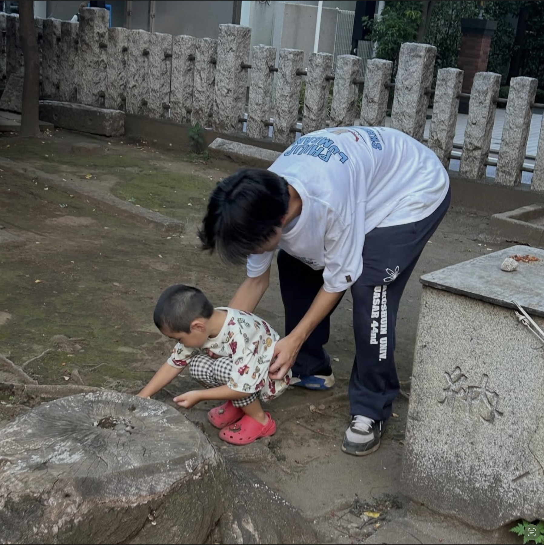 境内の石のくぼみをのぞく子どもにスタッフが寄り添うようす